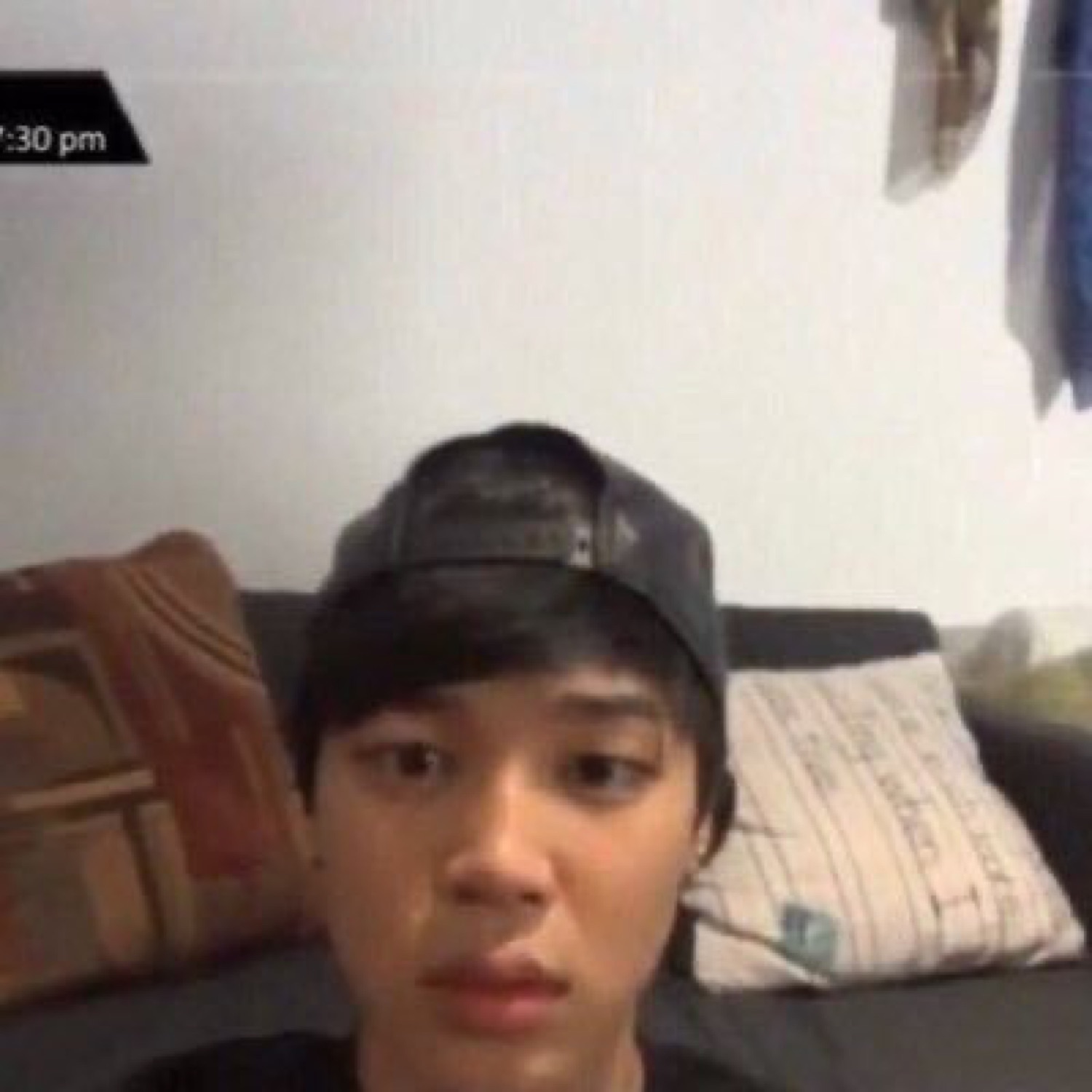 Young man in a backwards cap on a couch staring blankly at the camera at 7:30 pm