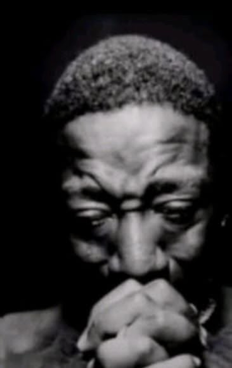 Man in black and white, head bowed with hands clasped, deep in thought or prayer