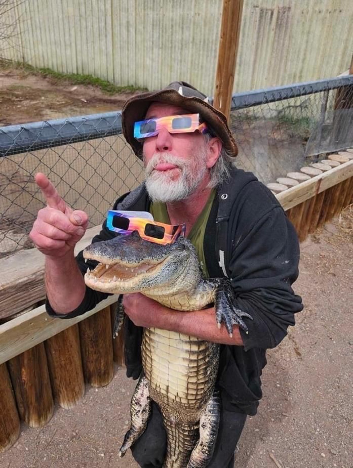Old man in 3D glasses pointing up while hugging an alligator that also wears 3D glasses