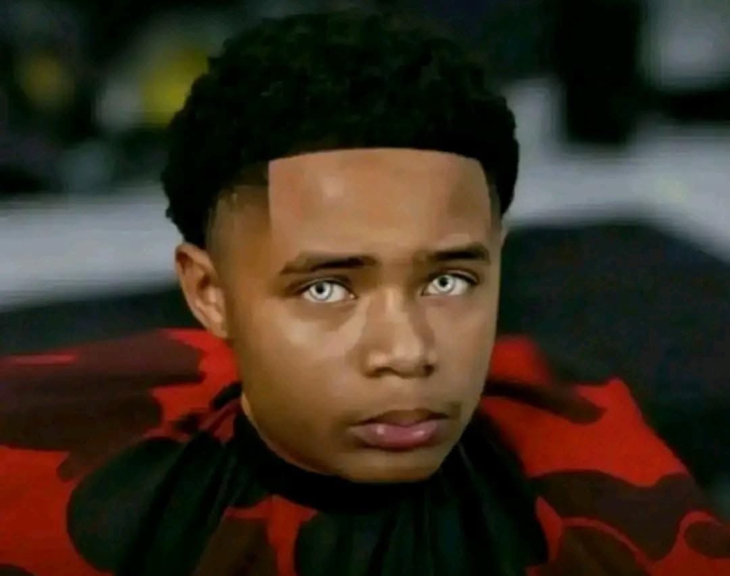 Young man in a barber cape staring blankly ahead with a deadpan expression