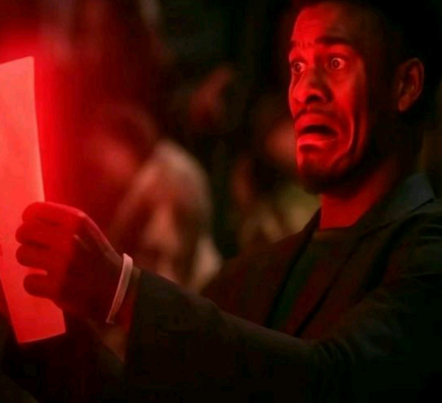 Man in red lighting reading a glowing paper with a horrified, terrified face