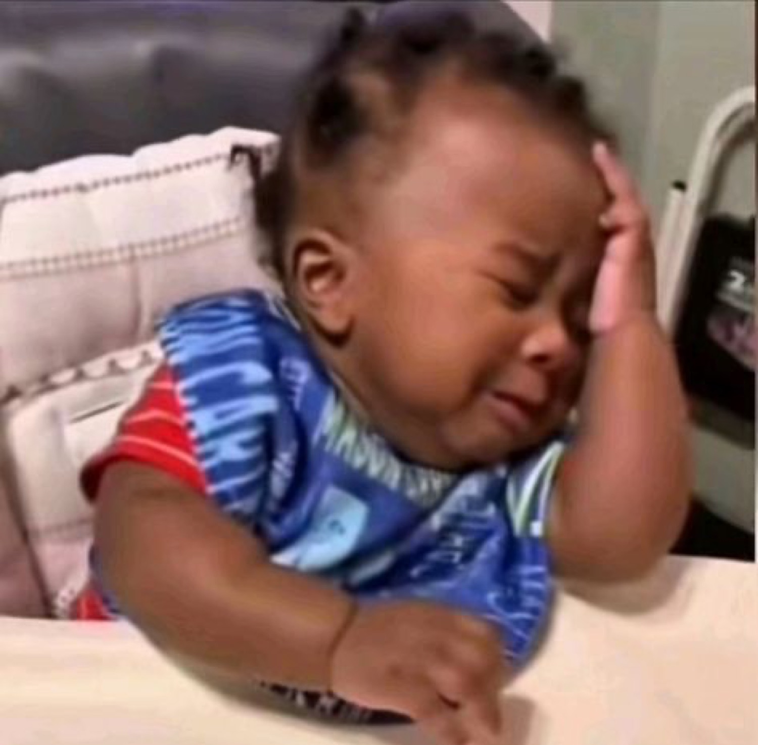 Baby in a high chair crying while holding their head in their hand like they've had enough