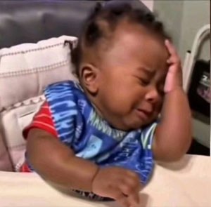Baby in a high chair crying while holding their head in their hand like they've had enough