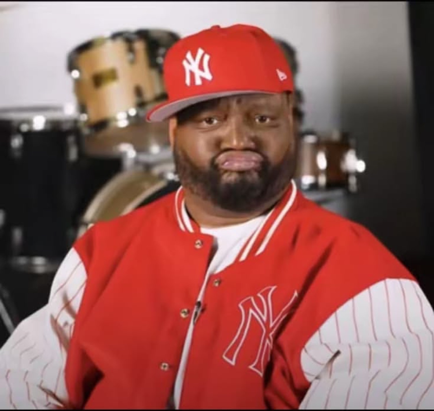 Man in a red Yankees cap and varsity jacket frowning