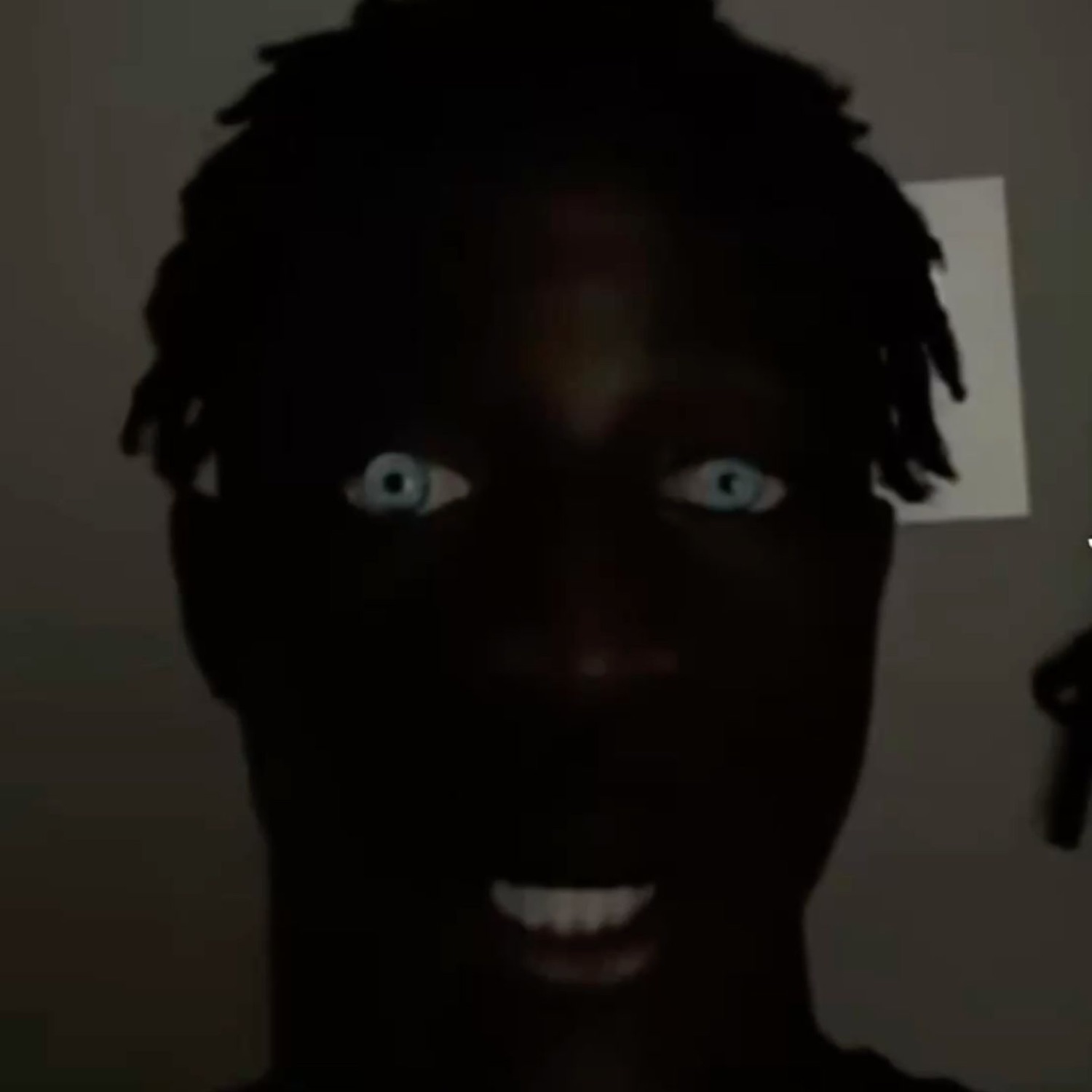 Man in a dark room with only his bright eyes and teeth visible, wide-eyed and startled