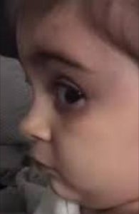 Baby in a car seat giving the most intense side-eye glance with one huge eye visible