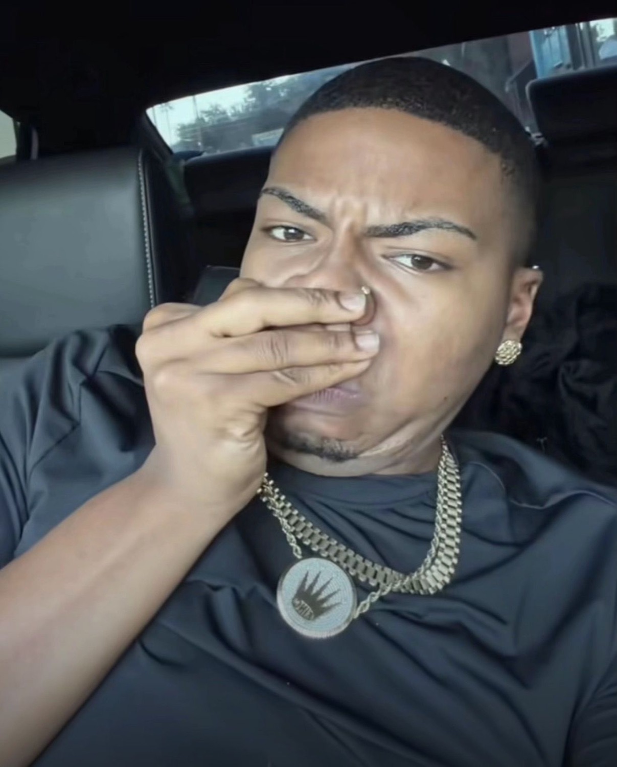 Man in a car covering his nose with a hand, giving a repulsed side-eye