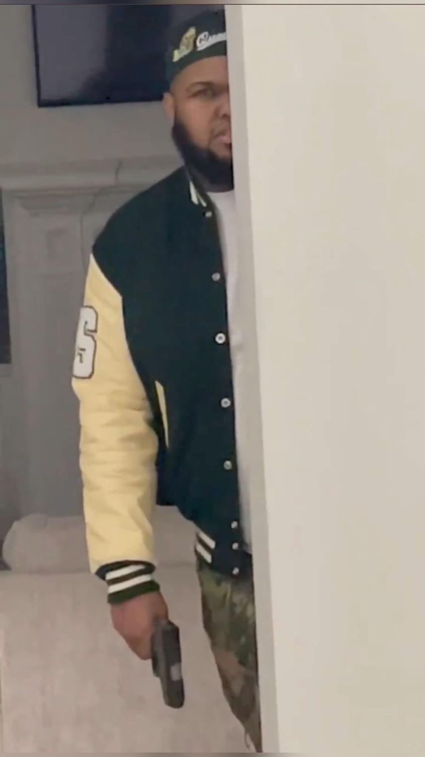 Man in a varsity jacket and cap peeking menacingly around a corner