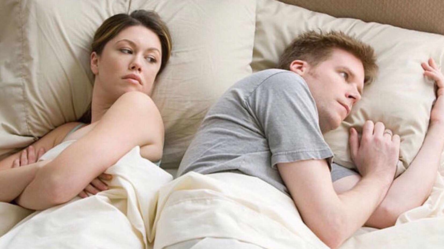 Couple in bed turned away from each other, both looking tense and unhappy