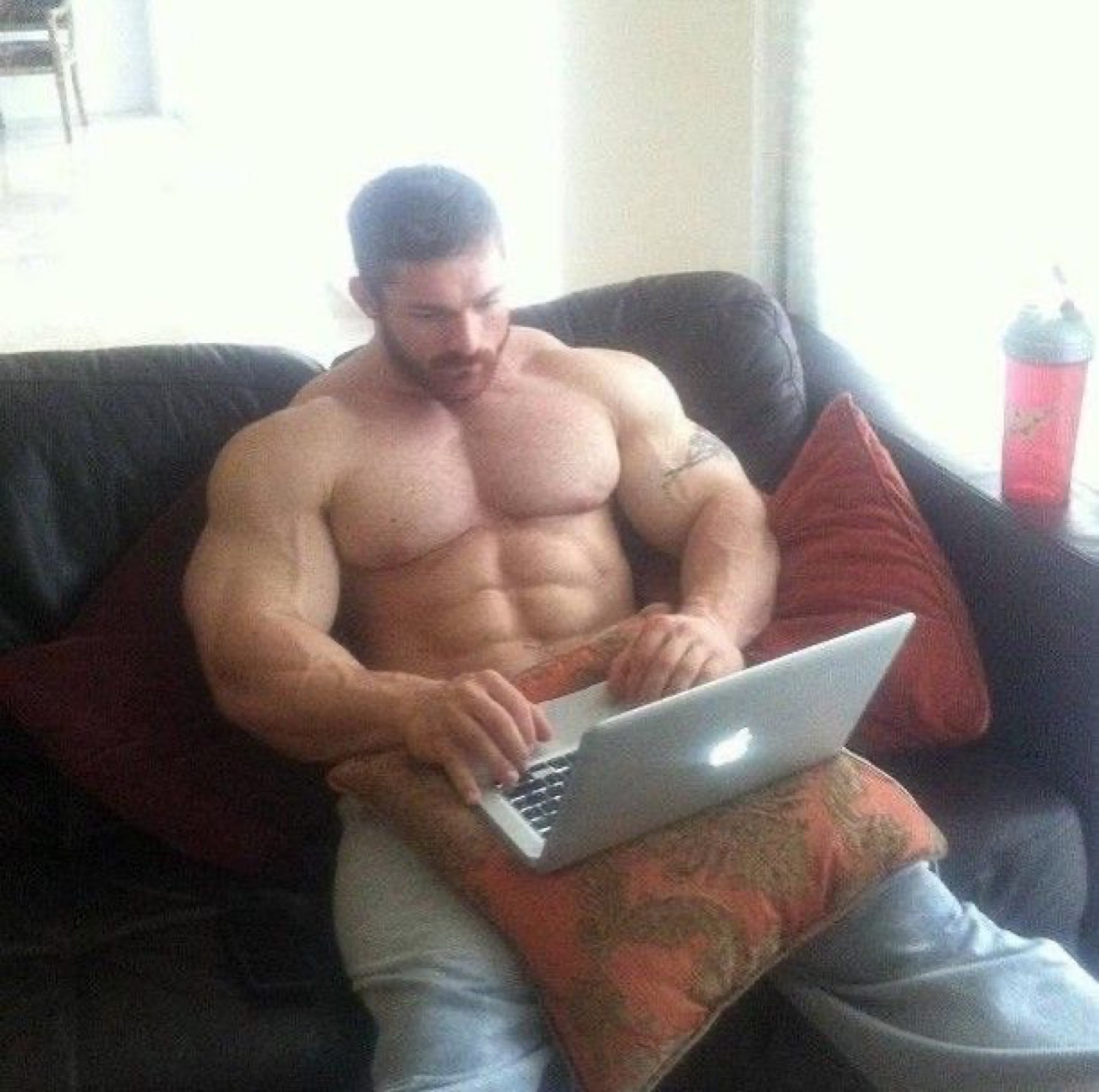 Huge bodybuilder sitting on a couch typing on a laptop