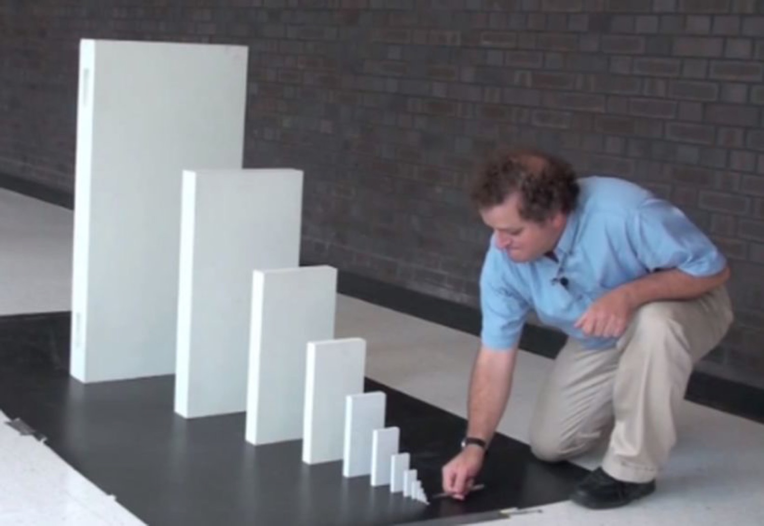 Man kneeling to topple a row of blocks that grow from tiny to enormous