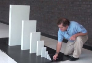 Man kneeling to topple a row of blocks that grow from tiny to enormous