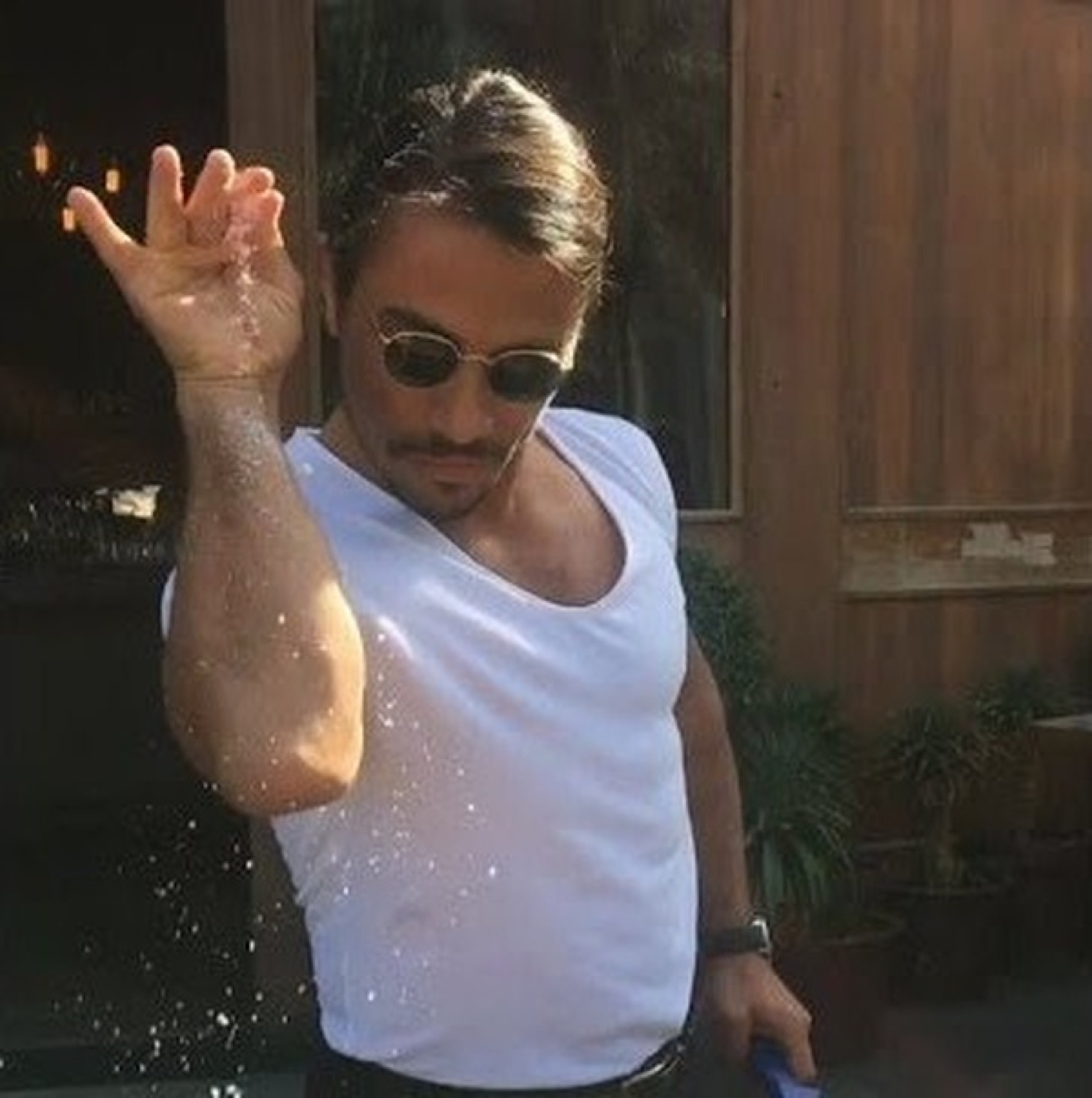 Salt Bae in sunglasses sprinkling salt down his forearm with signature flair