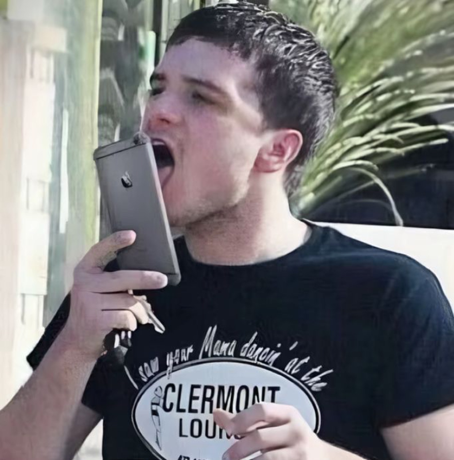 Guy dramatically opening his mouth wide to eat his phone outside a bar
