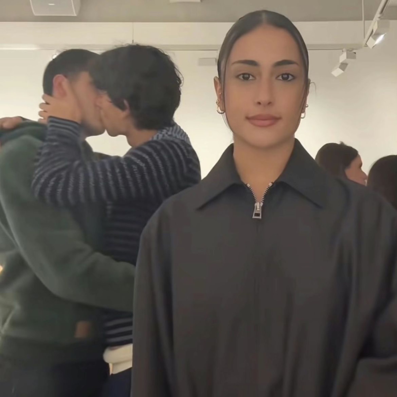 Woman staring blankly at the camera while a couple kisses behind her