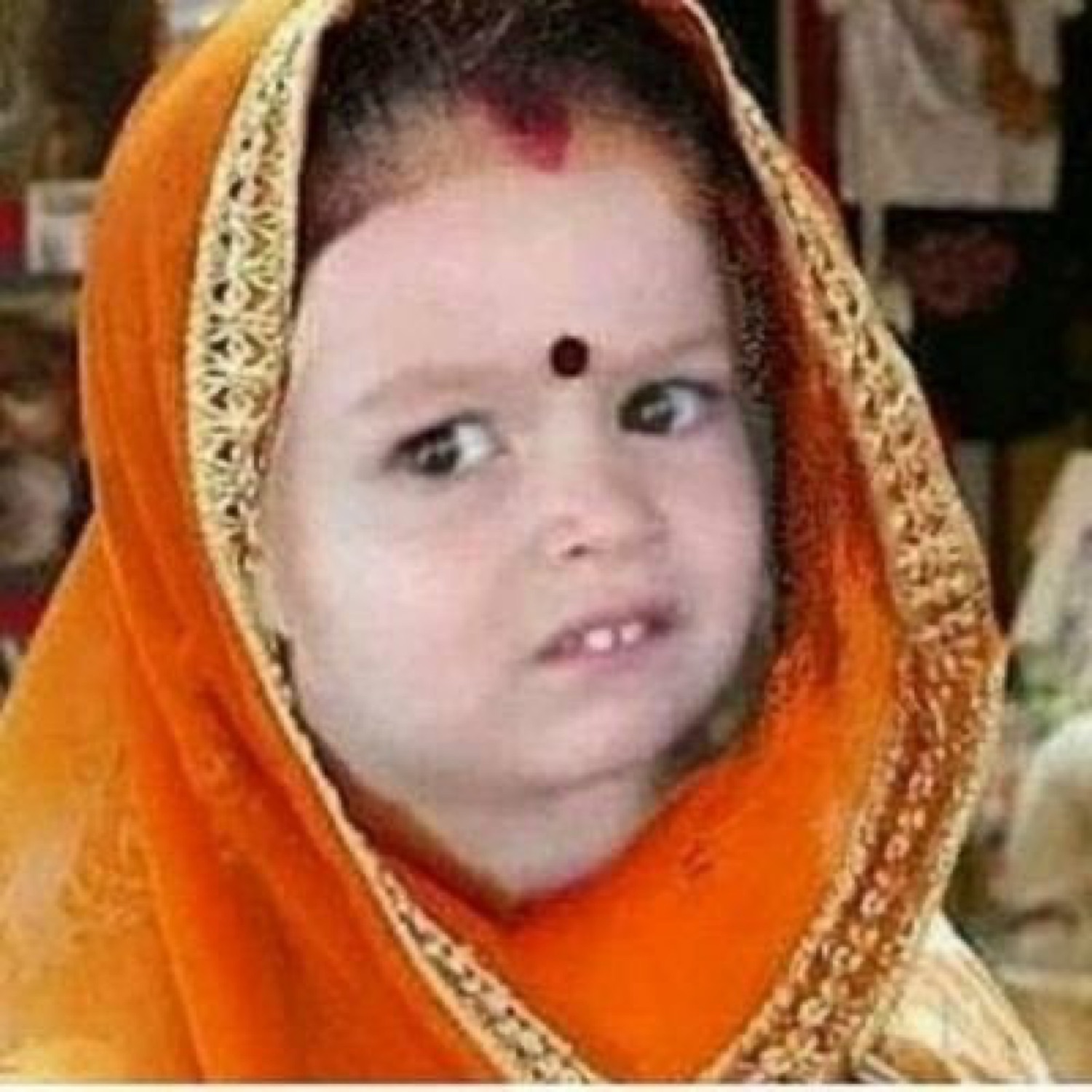 Little girl in an orange veil and bindi giving a suspicious side-eye