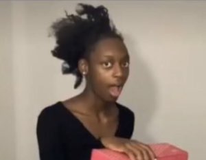 Young woman holding a pink gift box with her mouth wide open in surprise