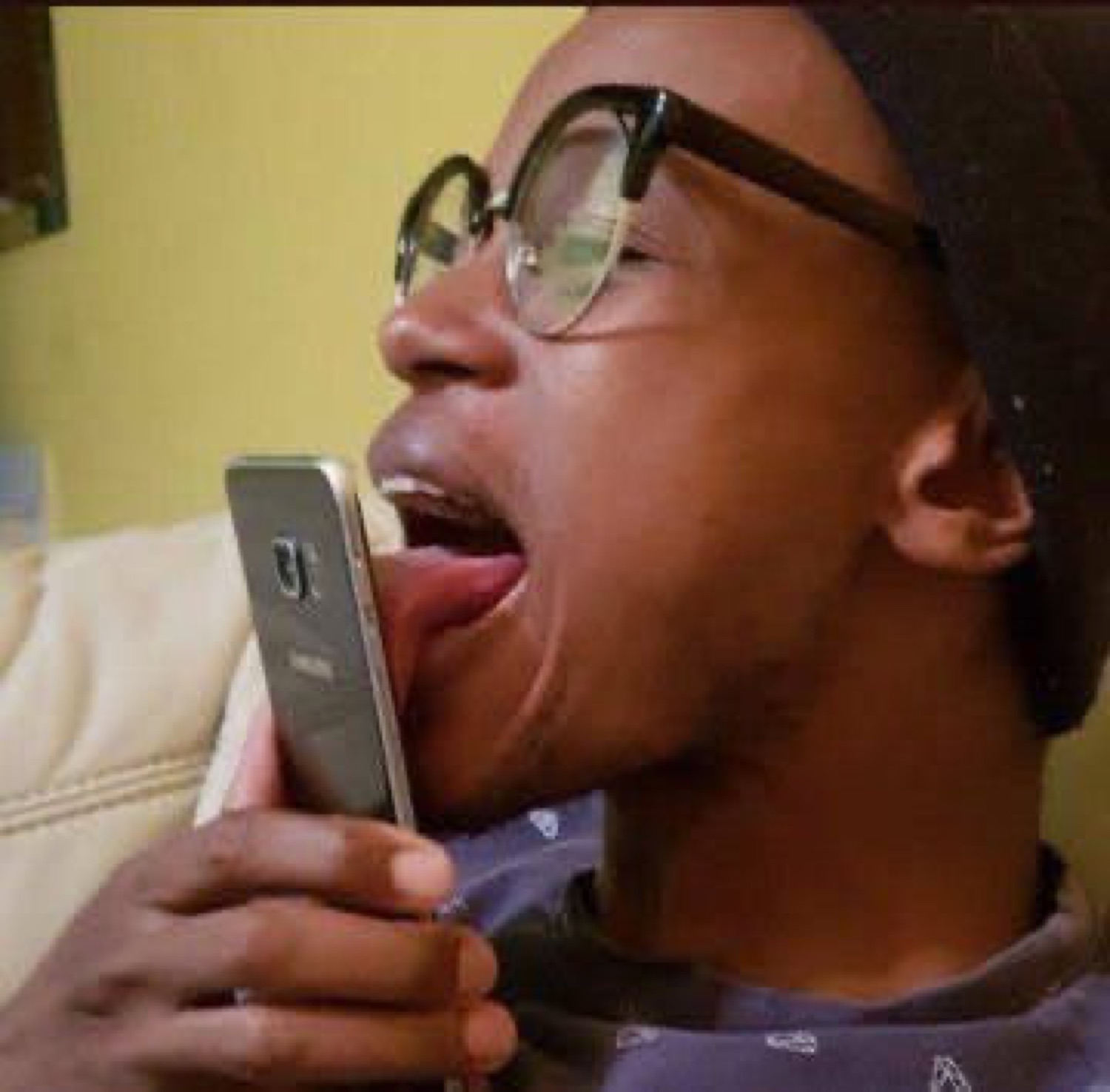 Guy in glasses and a beanie enthusiastically licking his phone screen