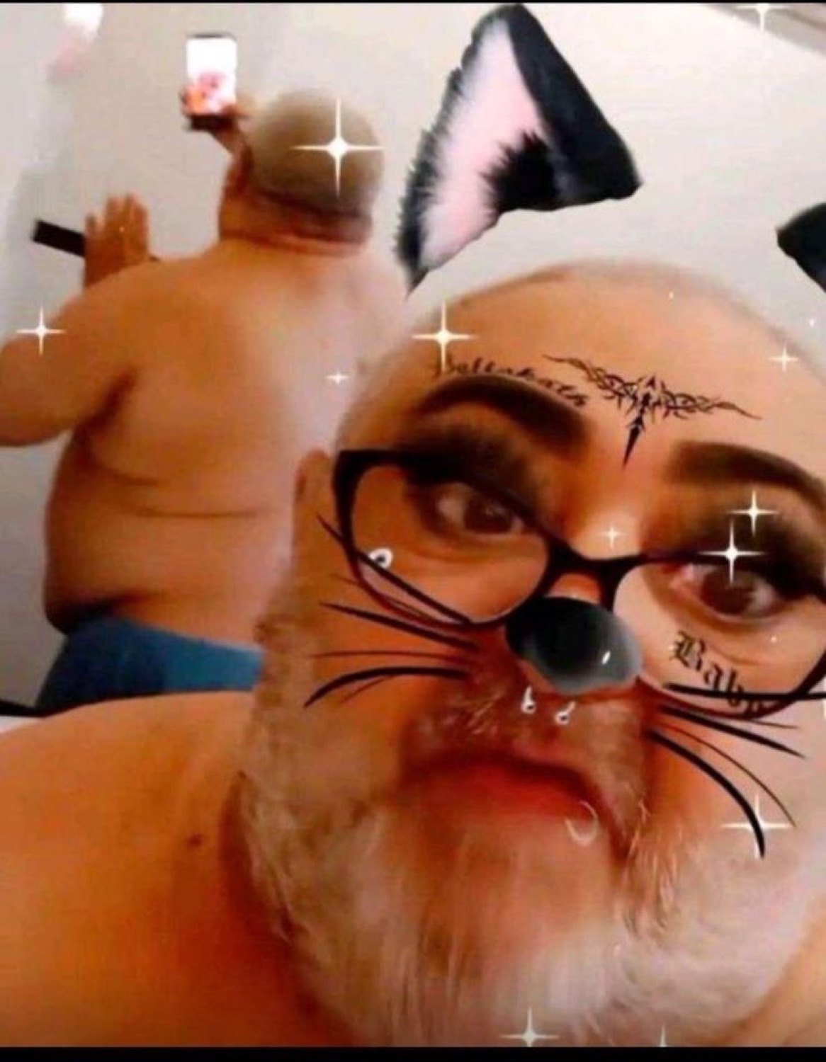 Bearded older man selfies with a cat-ears filter while a shirtless guy poses behind him