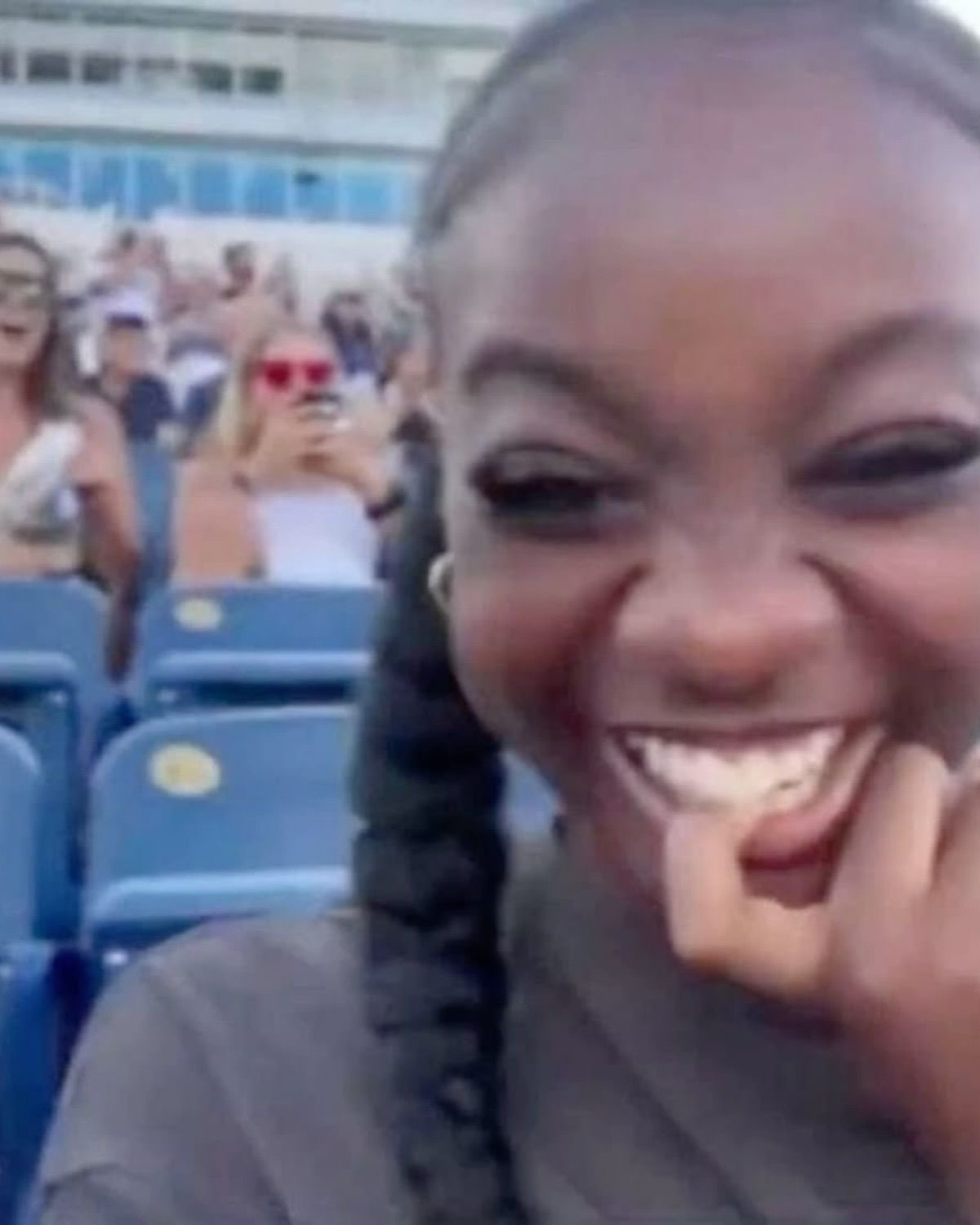 Girl in stadium seats cracking up with her hand on her chin