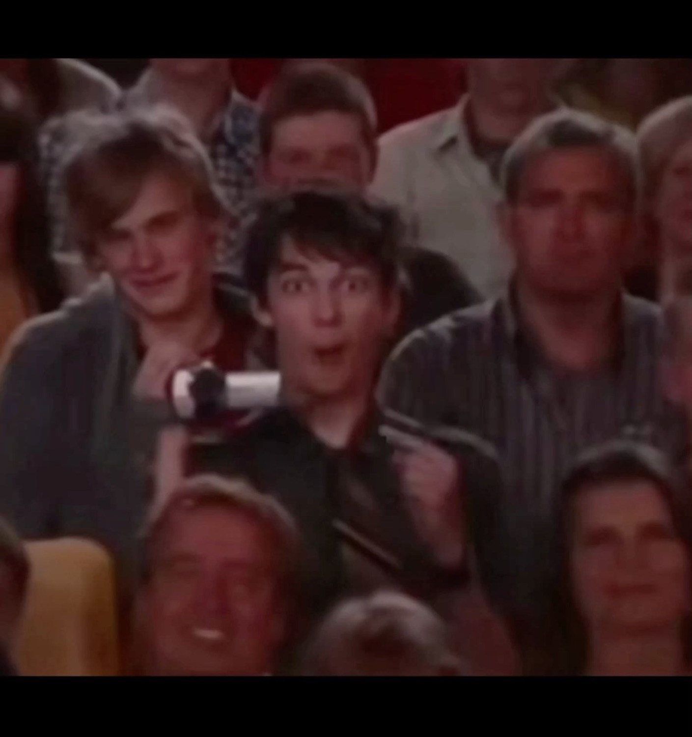 Young guy in a crowd pointing forward with a wide-eyed shocked and thrilled expression