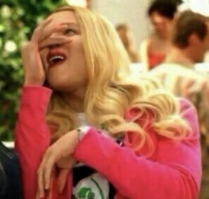 Blonde woman peeking through her fingers, laughing in disbelief