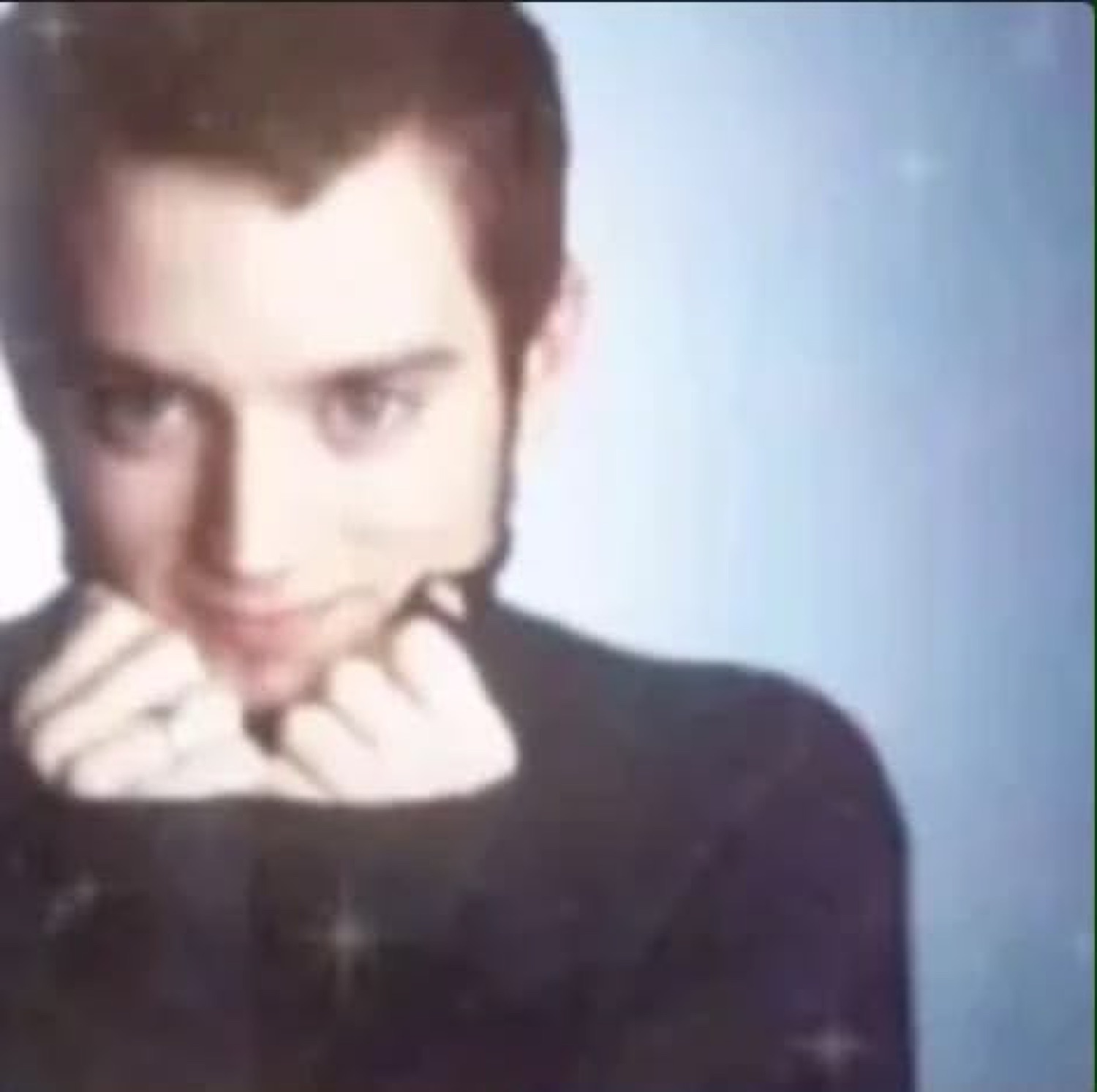 Young man with a subtle smirk and sparkle filter, chin resting on clasped hands
