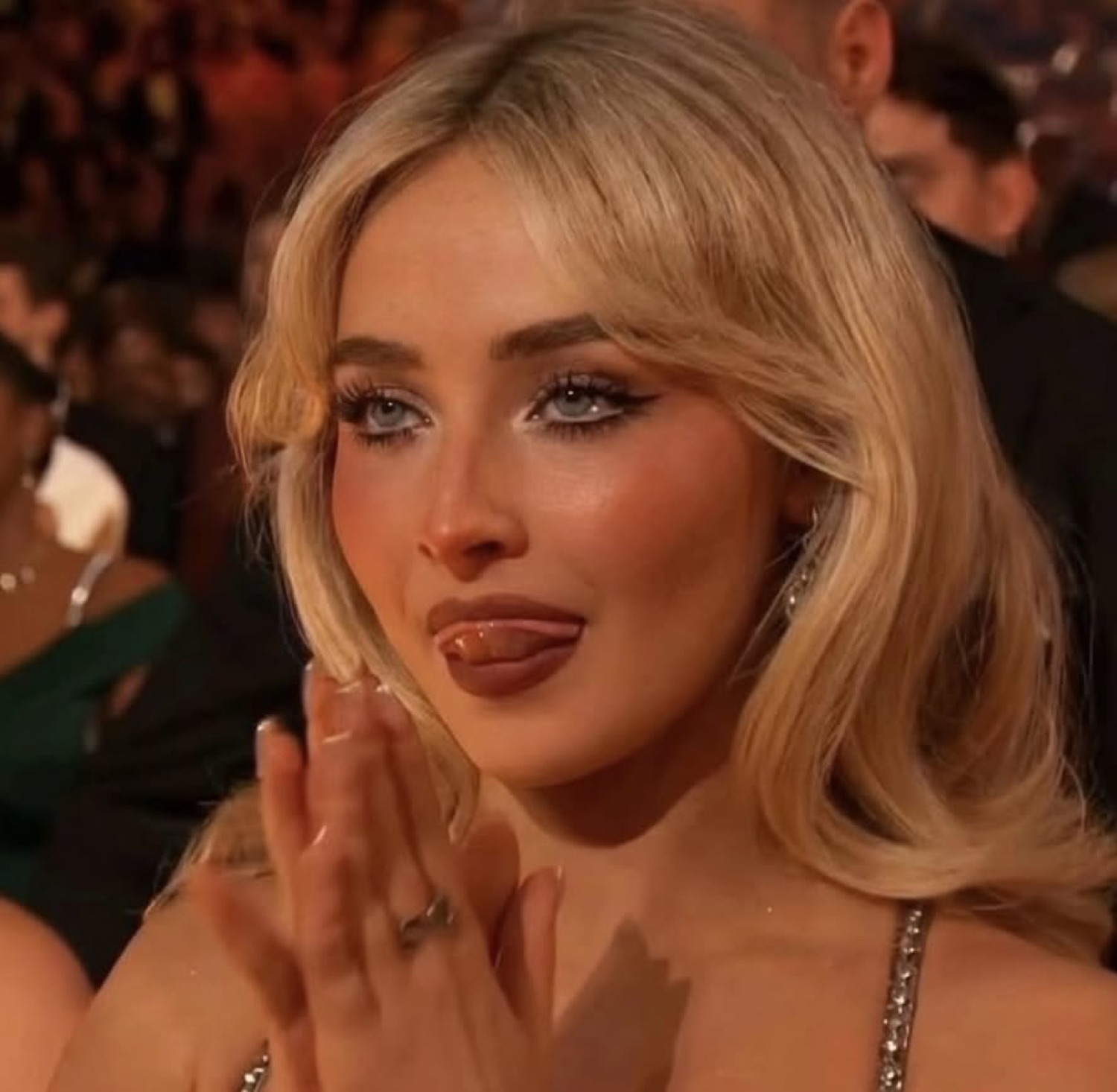 Blonde singer clapping at an awards show with her tongue stuck out