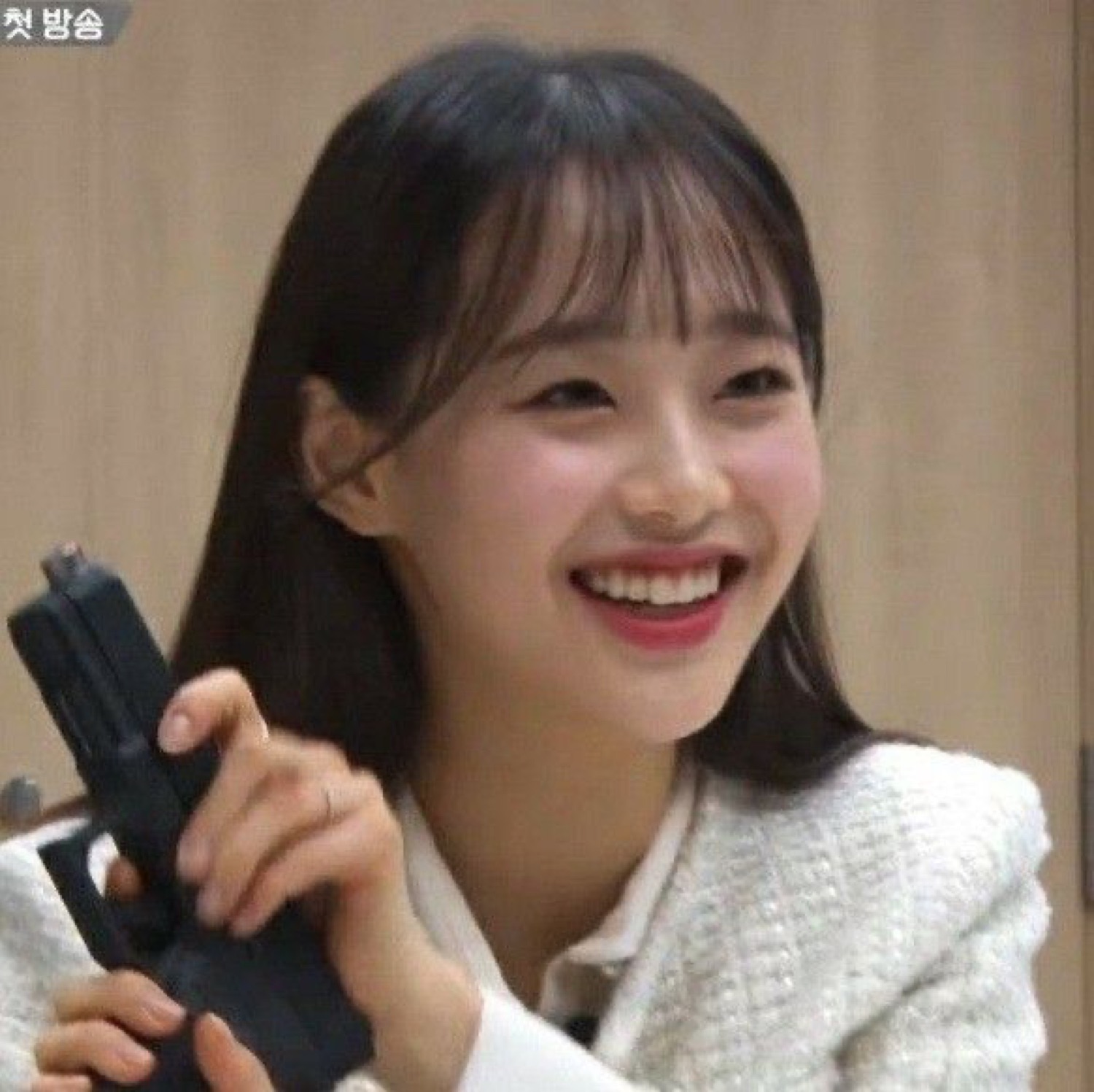 Smiling Korean woman in a white blazer casually holding a handgun