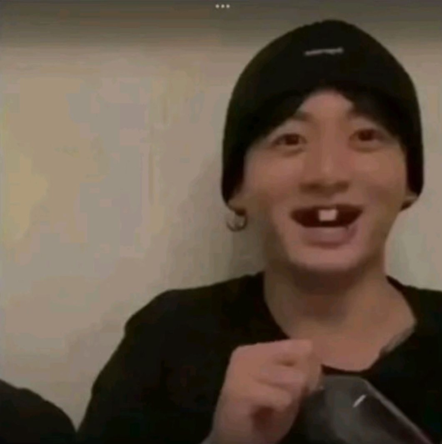 Young man in a black beanie laughing with a missing tooth, pointing at camera