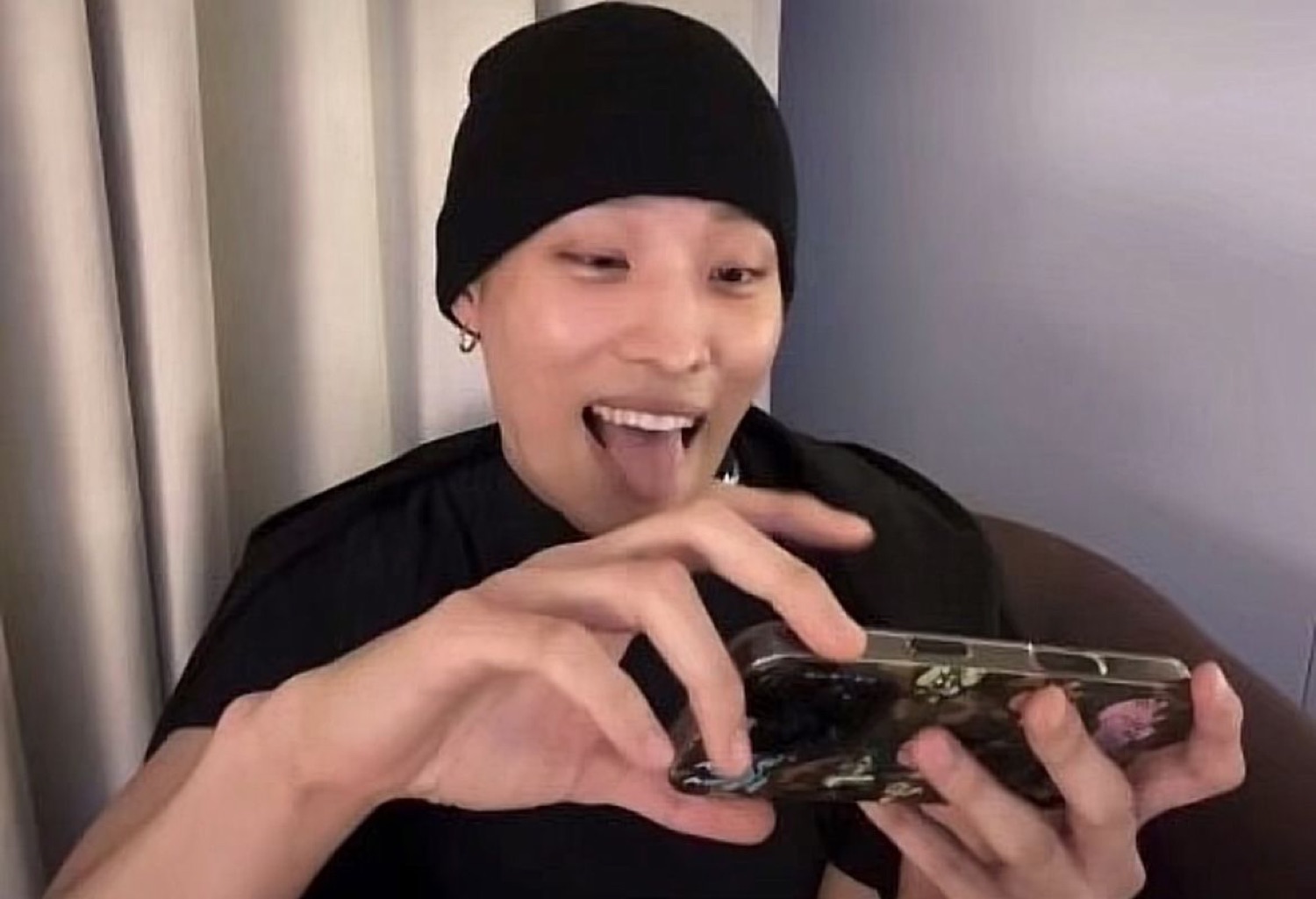 Person in a black beanie grinning with tongue out while frantically tapping their phone
