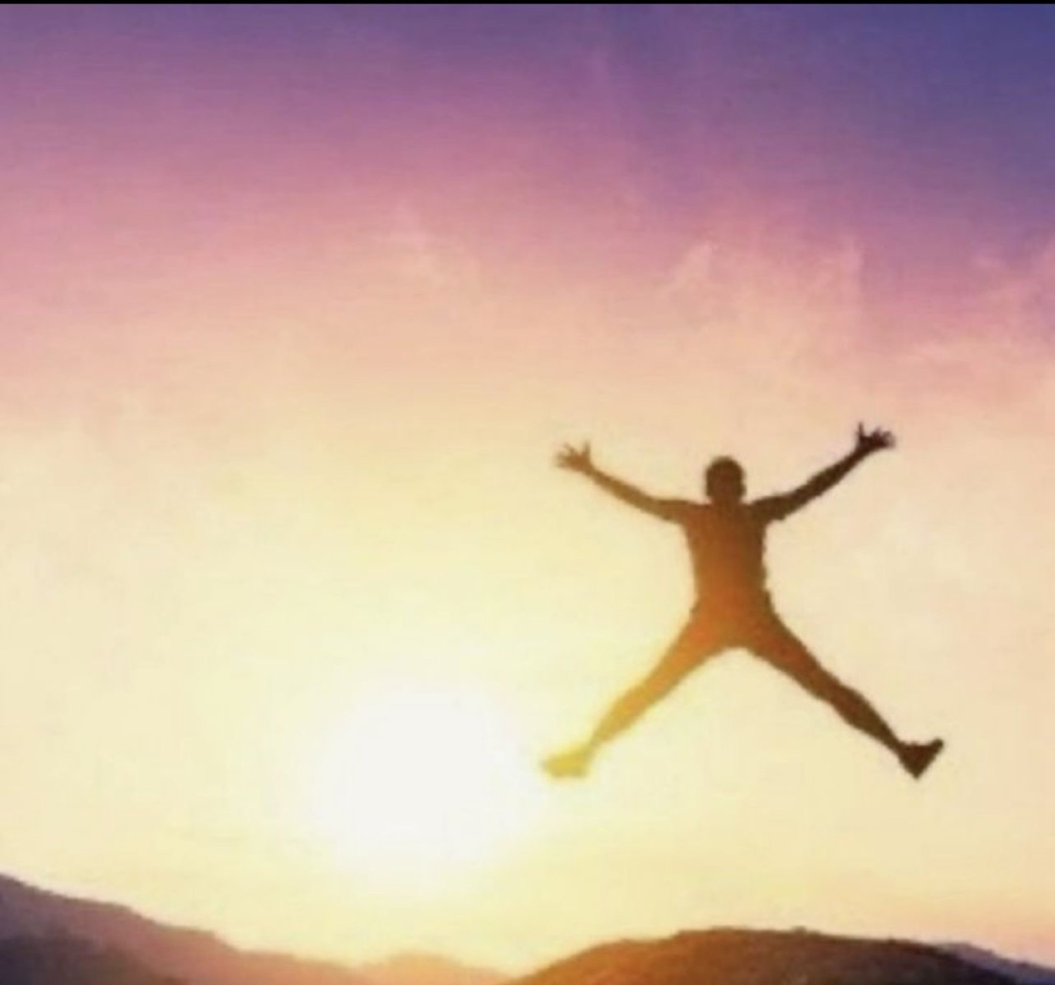 Silhouette of someone leaping arms-out against a glowing sunset sky