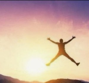 Silhouette of someone leaping arms-out against a glowing sunset sky