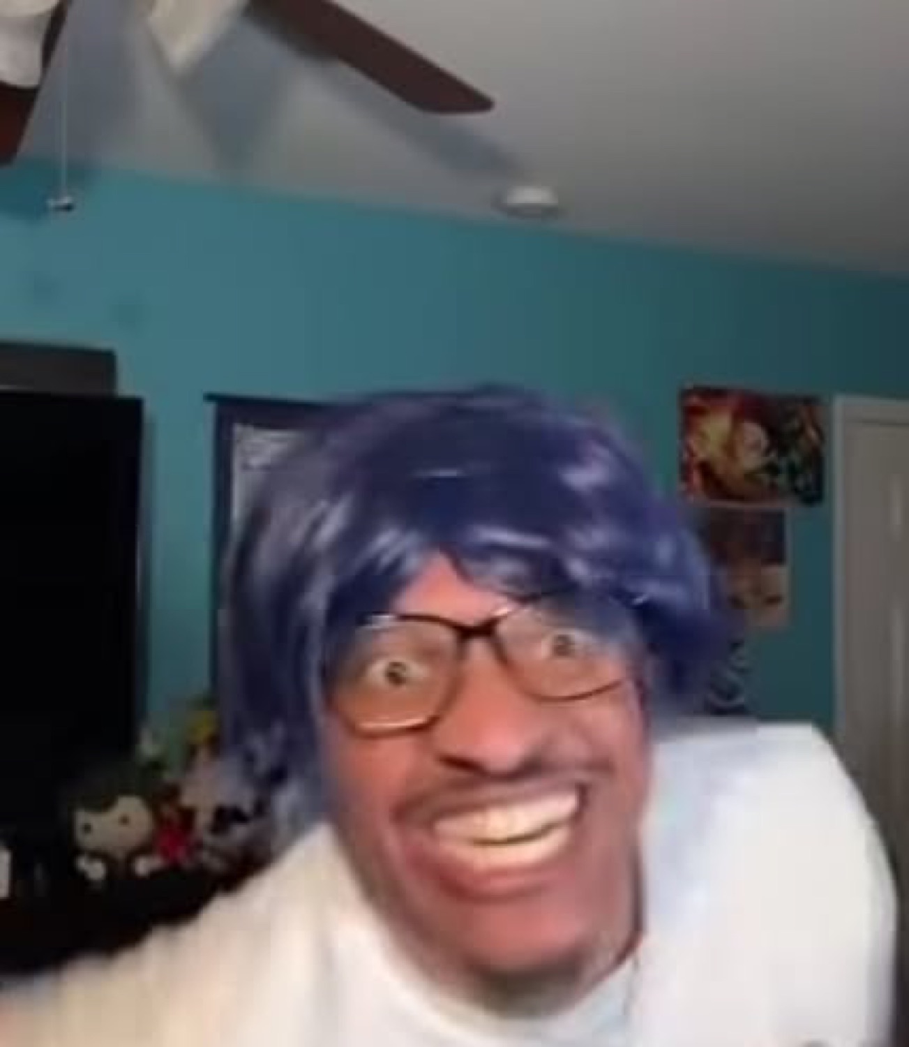 Man in a blue wig and glasses pulling a wild, wide-eyed manic grin