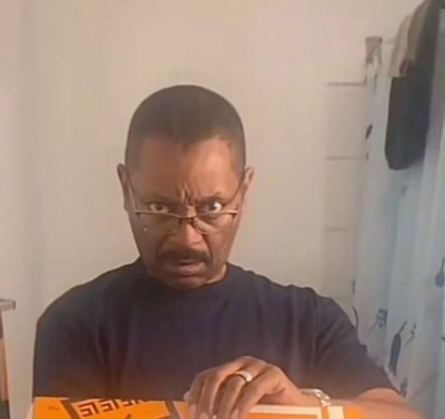 Older man glaring intensely over his glasses while working at a table