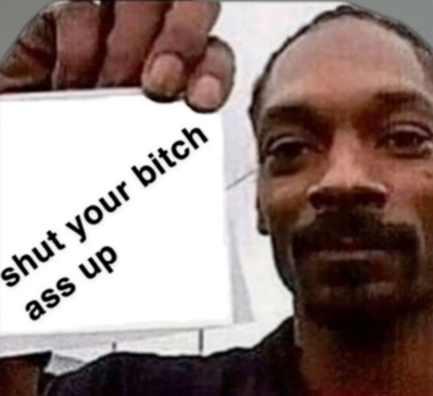 Snoop Dogg holding up a sign reading 'shut your bitch ass up' with a calm unbothered face