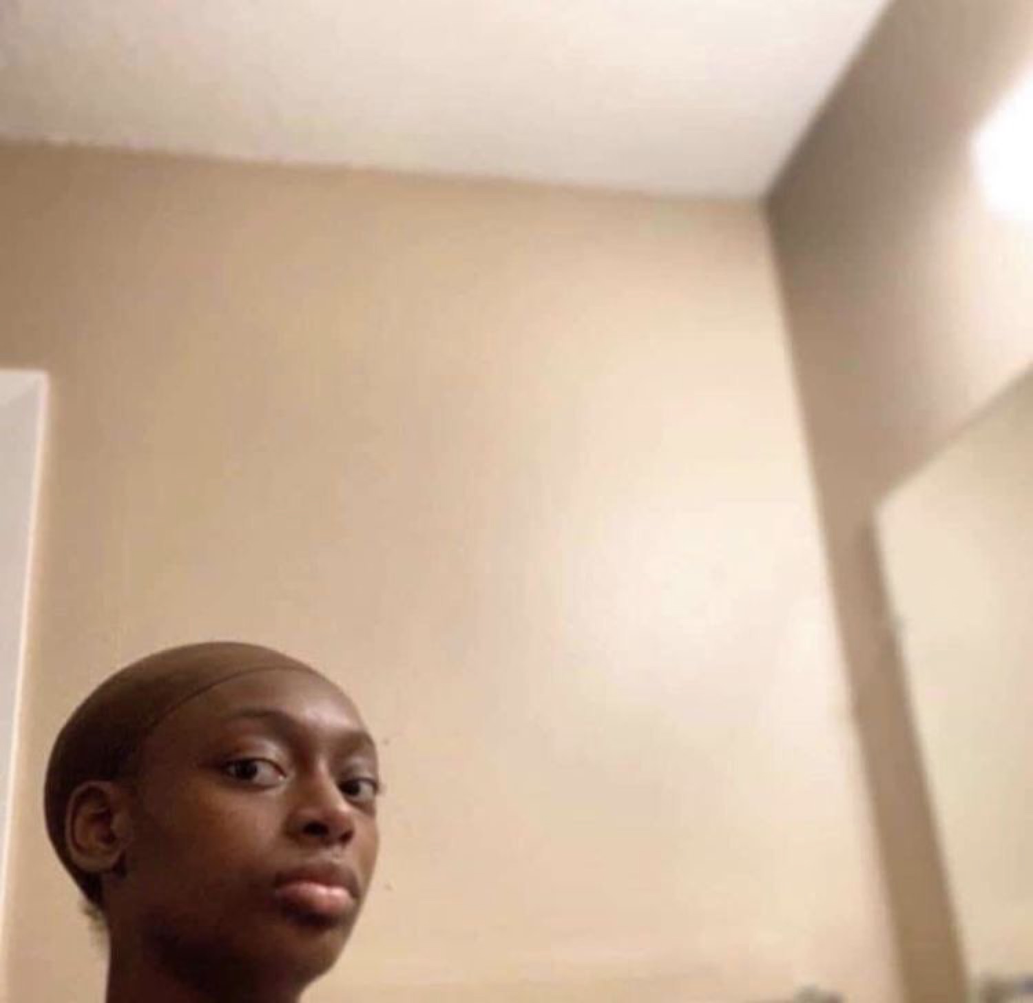 Person peeking into the bottom of a bathroom-selfie frame with a flat, deadpan look