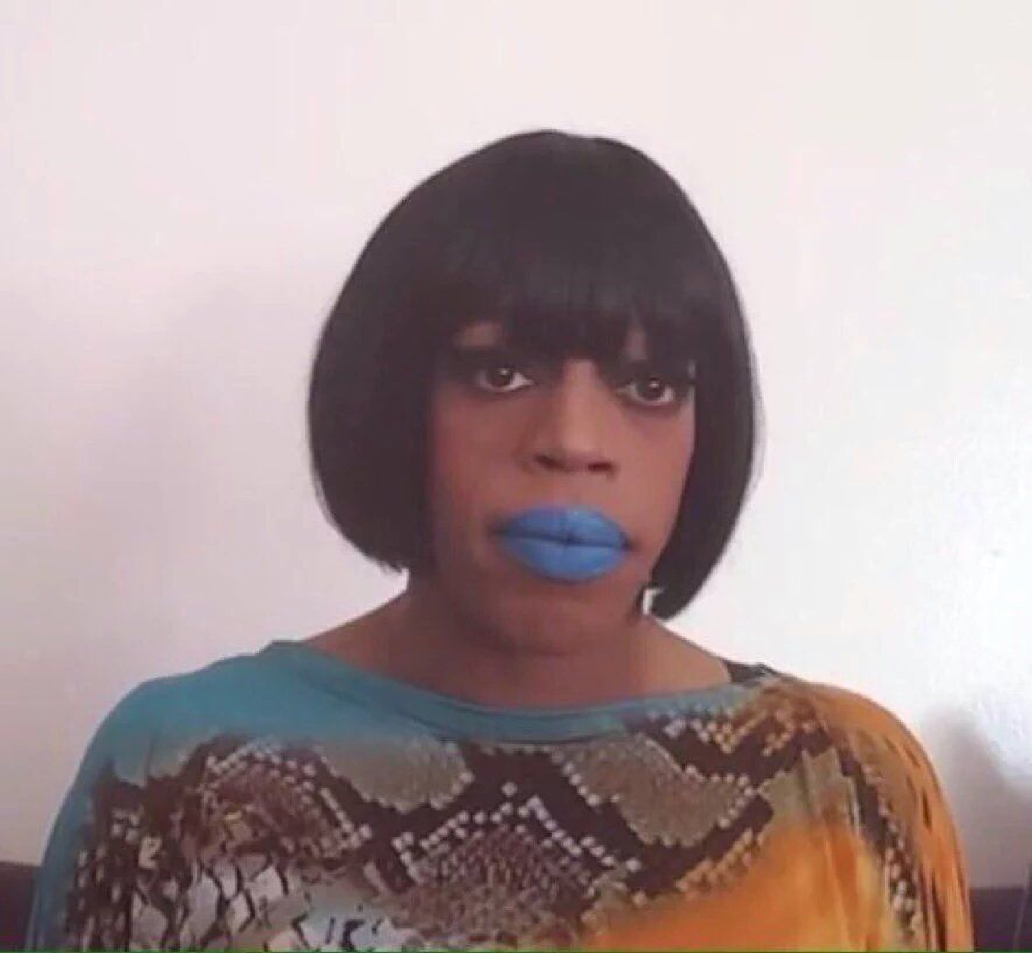 Person in a bob wig and bright blue lipstick staring down the camera deadpan