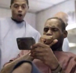 LeBron squinting at his phone while a teammate behind him reacts with mouth wide open