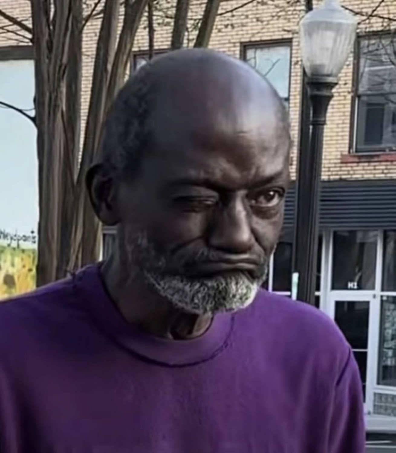 Man in a purple shirt outdoors throwing a heavy, unimpressed side-eye