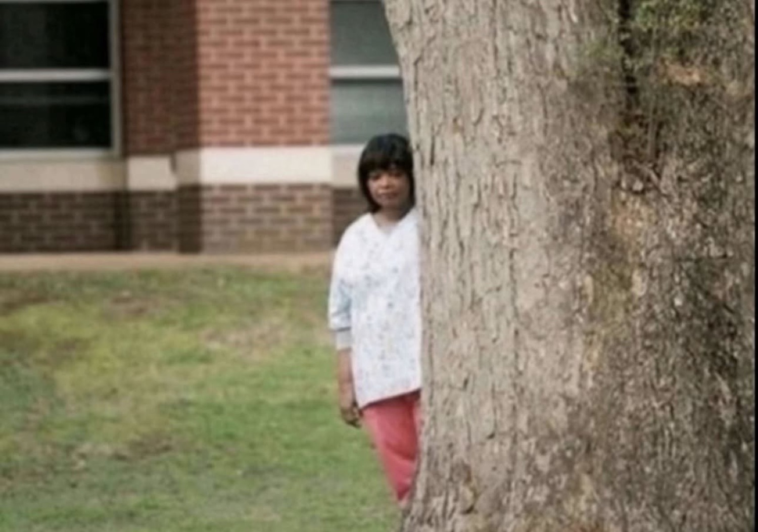 Woman half-hidden behind a tree, peeking out awkwardly at the camera