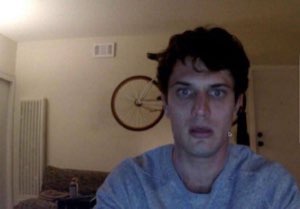 Man on a webcam staring wide-eyed and stunned in his apartment