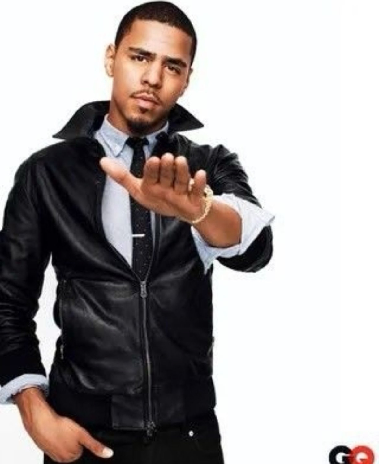 Man in a leather jacket reaching a hand toward the camera with a cool deadpan stare