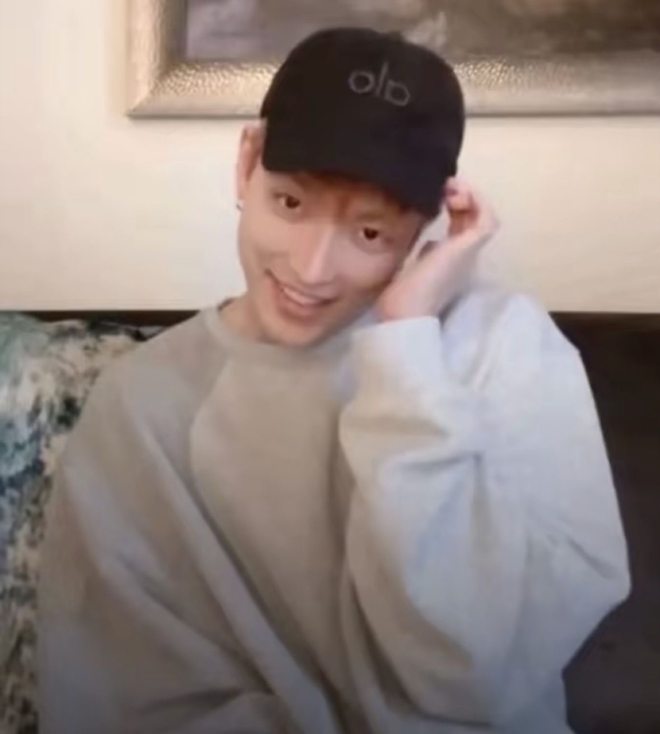 Guy in a black cap smiling shyly with a hand tucked behind his ear