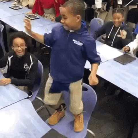 Boy in a navy hoodie dancing in a classroom while classmates watch