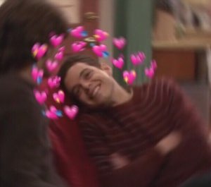 Grinning man mid-hug swarmed by a ring of pink heart emojis