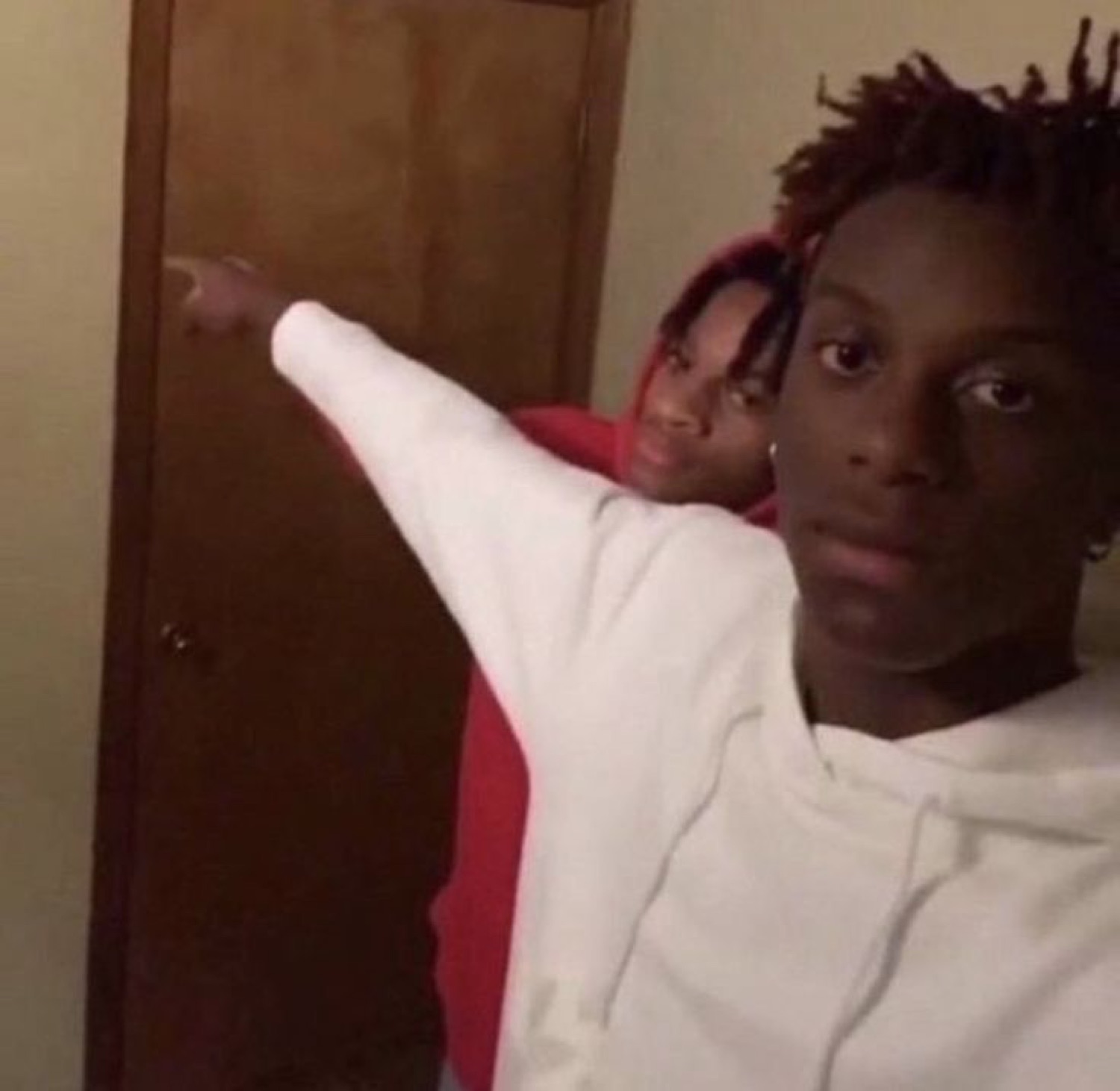 Guy in a white hoodie pointing flatly at the door while someone smirks behind him