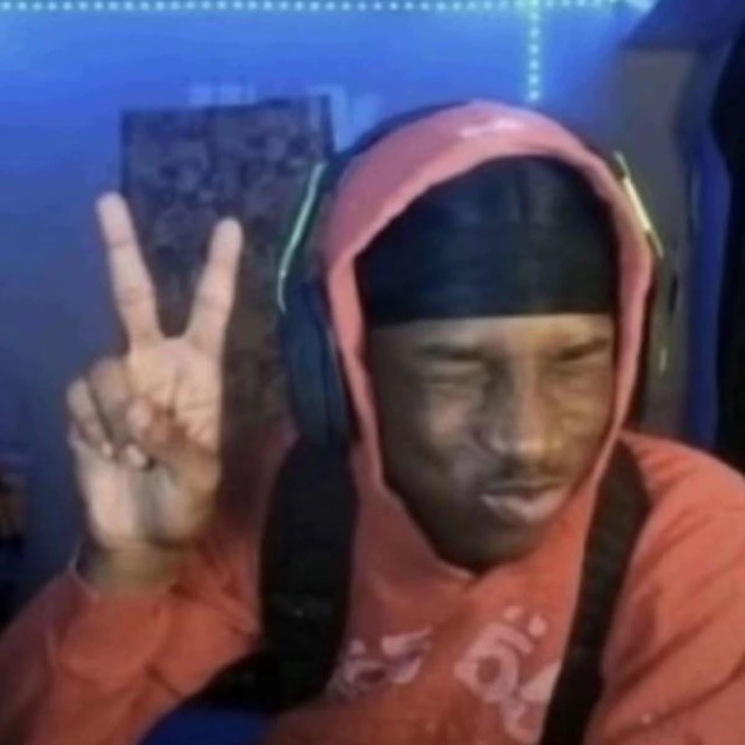 Guy in a hoodie and headphones throwing a peace sign with his eyes closed