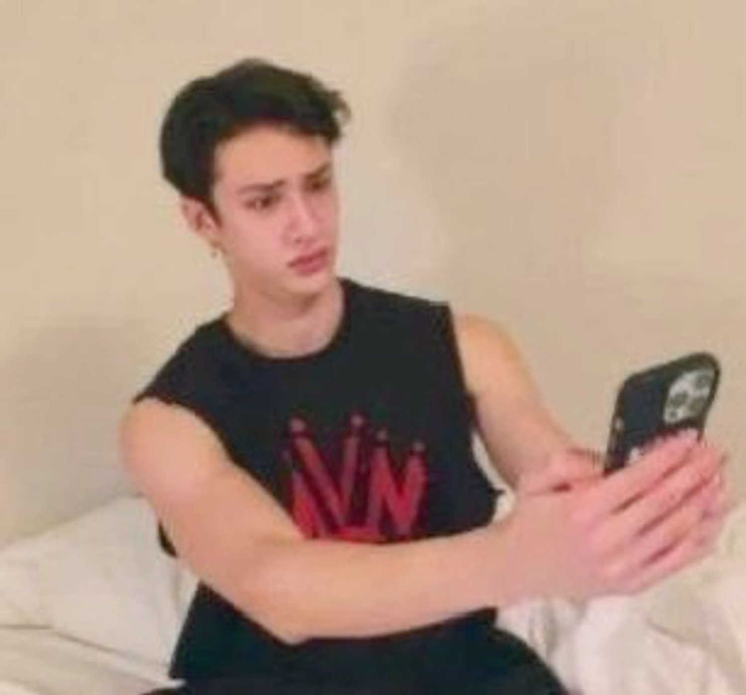 Young man sitting on a bed filming himself with a flat, disappointed frown