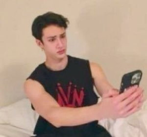 Young man sitting on a bed filming himself with a flat, disappointed frown